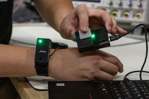A researcher transfers information from a chip in a watch by touching a sensor connected to a laptop